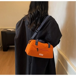 Detail of orange nylon crossbody bag with zipper pocket and adjustable strap worn by model