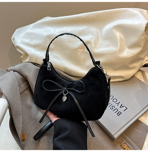 Detail van zwarte suède hobo tas met een strik en een zilverkleurige hart hanger