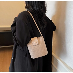 Detailed view of beige woven leather bucket bag with a round buckle and strap on model