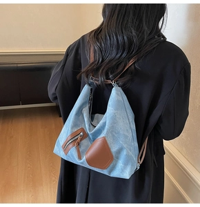 Detail view of light blue denim backpack with brown leather trim and contrast straps