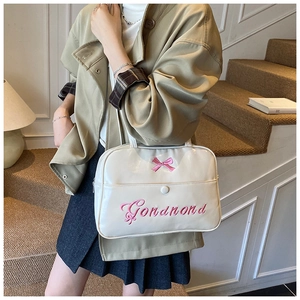 Close-up of beige patent leather bag featuring pink bow embroidery and front pocket detail