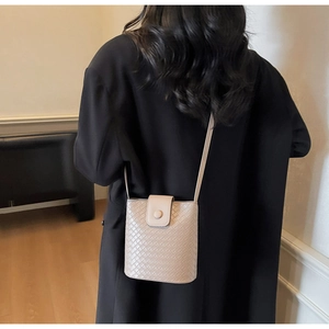 Detail of beige woven leather bucket bag with magnetic flap worn over a black coat