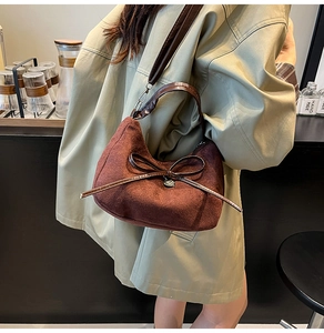 Detail van donkerbruine suède handtas met strik gedragen bij een trenchcoat in een café
