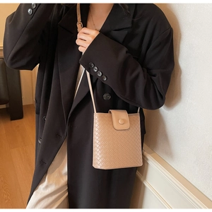 Detail of a beige woven leather crossbody bucket bag with textured flap and round buckle