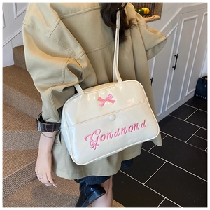 Detail of cream shoulder bag featuring pink bow embroidery and glossy faux leather texture