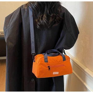 Detail view of bright orange nylon crossbody tote with blue adjustable shoulder strap