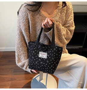 Close-up of black corduroy tote bag with white bow patterns and heart prints