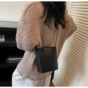 Detail of black woven texture bucket bag with snap closure on a model in a warm setting