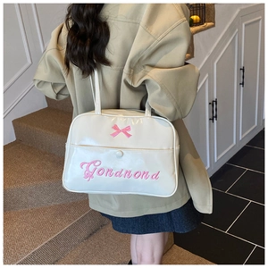 Detail of cream-white leather shoulder bag with pink bow embroidery on a model