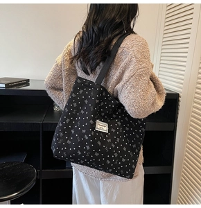 Close-up of black corduroy tote bag with white heart and bow patterns on shoulder strap