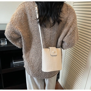 Close-up of white woven leather bucket bag worn by model with textured cross-body strap