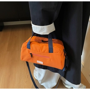 Detail of vibrant orange nylon tote bag with JL FASHION label and blue handles