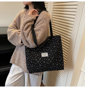 Detail of black canvas tote bag with heart and bow patterns on model in cozy home setting