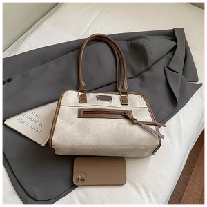 Détail d'un sac fourre-tout en toile avec finitions en cuir brun et pompon sur blazer