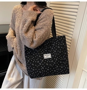 Detail of black corduroy tote bag featuring white heart and bow prints on wide shoulder strap