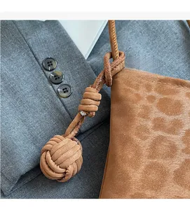 Detail shot of a brown suede handbag with a decorative woven knot and textured strap