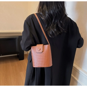 Detailed view of brown woven bucket bag with long strap worn over a black blazer