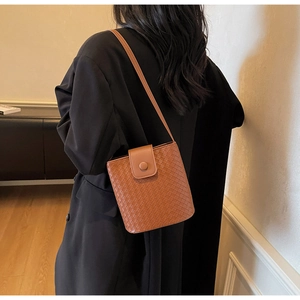 Detail of caramel brown woven bucket bag with elegant metal buckle on stylish model