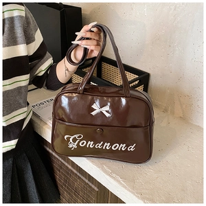 Detail of dark brown glossy patent leather shoulder bag with white bow and embroidery