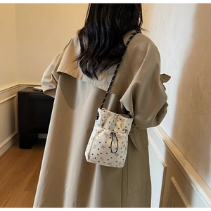 Detail of pleated corduroy phone bag with bow patterns worn by a model in a trench coat