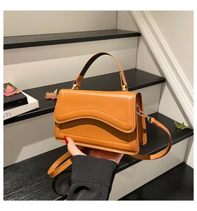 Detail view of caramel brown leather handbag with wavy stitching on a staircase