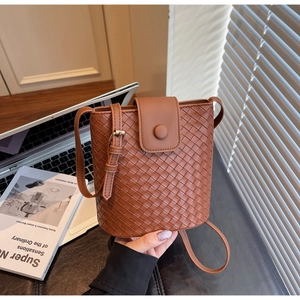 Detail of a brown woven leather bucket bag featuring a minimalist buckle and adjustable strap