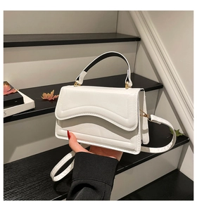 Detail of white leather crossbody bag featuring wave-shaped flap and golden metal hardware