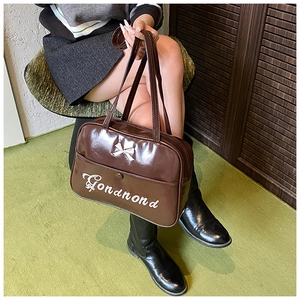 Detail of dark brown glossy shoulder bag with silver bow accent and white lettering