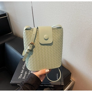 Detail of light green woven mini bucket bag featuring intricate weave texture and gold buckle