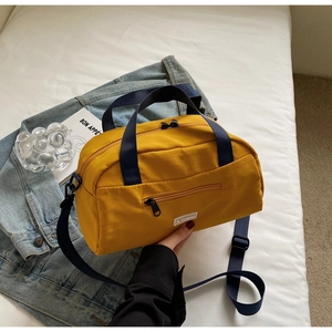 Detail of yellow nylon Boston bag with blue webbing handles on a white background