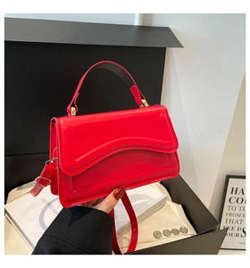 Detail of red glossy leather handbag with wavy stitching and adjustable shoulder strap