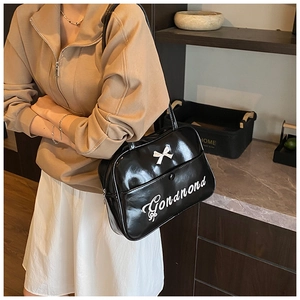 Detail of black glossy patent leather shoulder bag with white bow and cursive text