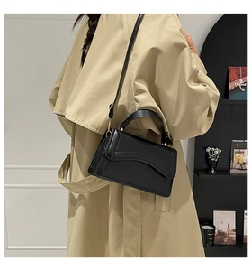 Detail of black leather square bag with wave flap and gold buckle on a stylish model