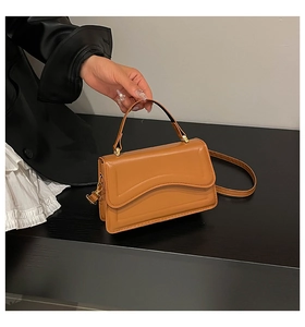 Detail of caramel brown handbag featuring wavy flap design and gold hardware