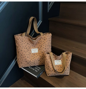 Detail of tan corduroy tote bags with black heart patterns and branded cloth labels