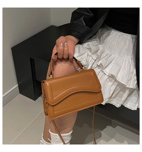 Detail of a brown leather bag with a wavy flap and golden cylindrical metal hardware