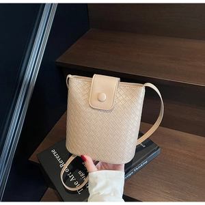 Detail of beige woven bucket bag with leather magnetic flap and slim shoulder strap