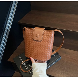 Detail of a brown woven bucket bag with a flap closure on wooden stairs
