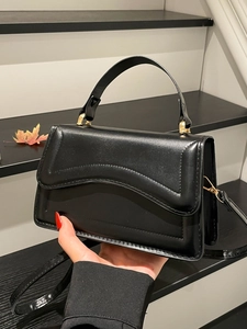 Minimalist black handbag with wavy stitching and gold hardware shown in an indoor setting