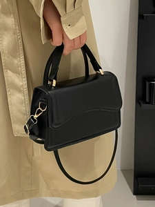 Minimalist black leather handbag with gold metal clasp on a beige coat background