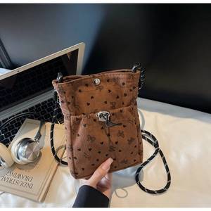 Detail of brown corduroy phone bag with heart and bow patterns on a cozy desk setup