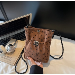 Close-up of brown corduroy crossbody bag with bow prints and woven rope strap