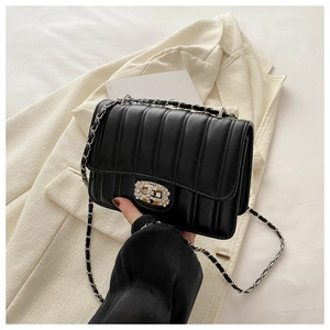 Detailed view of black quilted crossbody bag with rhinestone buckle and chain strap
