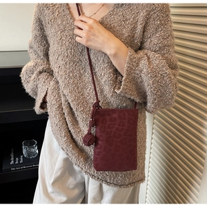 Detail of burgundy leopard embossed phone bag with elegant sphere knot charm decoration