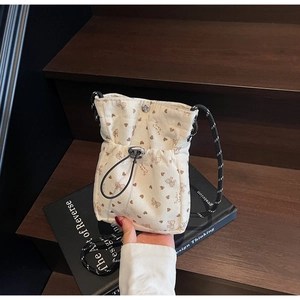 Detail of cream corduroy crossbody bag with brown heart patterns and black drawstring closure