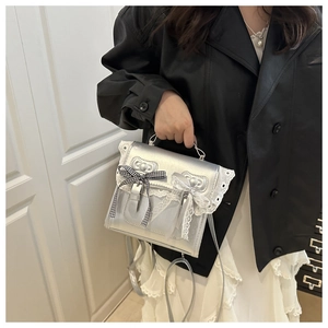 Détail du sac argenté métallisé avec bordures en dentelle et nœuds sur fond de porte blanc