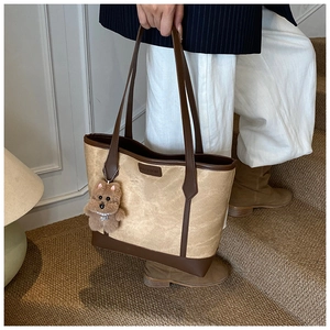 Detail of khaki tote bag with brown leather trim and cute plush puppy charm on stairs