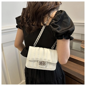 Detail of white quilted chain bag with rhinestone lock worn on a black dress