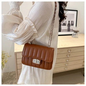 Close-up of brown quilted chain bag with rhinestone lock worn on a white blouse