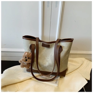 Detail of sage green tote bag with brown leather trim and cute puppy charm on white fabric